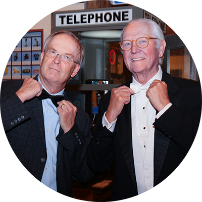 two men in tuxedos posing in front of phone booth